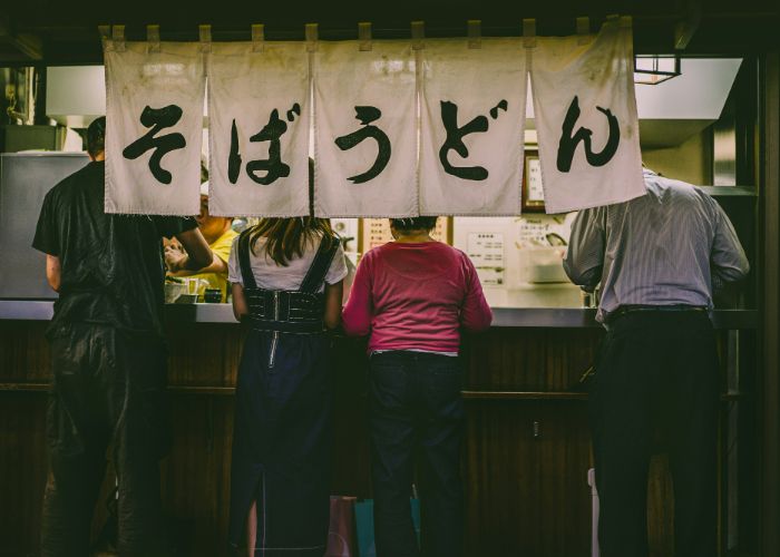 A soba and udon stall in Japan, with four people eating at the counter.